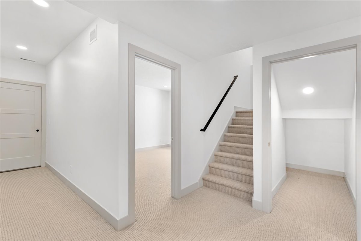 Carpeted staircase with black handrail, leading to a light-filled upper level