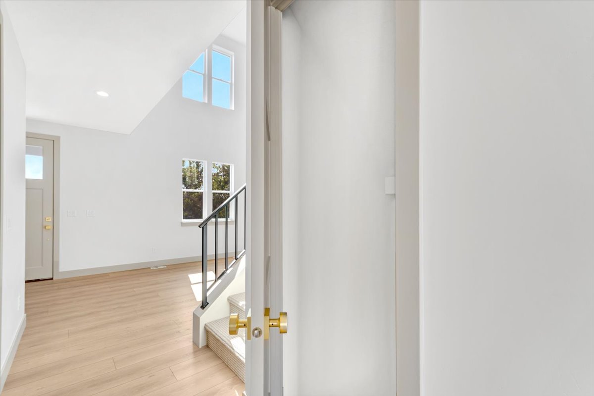 Foyer featuring soaring vaulted ceilings, multiple windows, light wood-finish flooring, and a staircase with a black metal railing