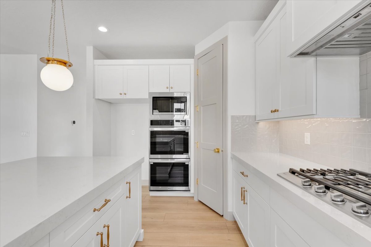 Modern kitchen featuring white cabinetry, light countertops, wood-finish flooring, a gas cooktop, and a built-in oven and microwave stack