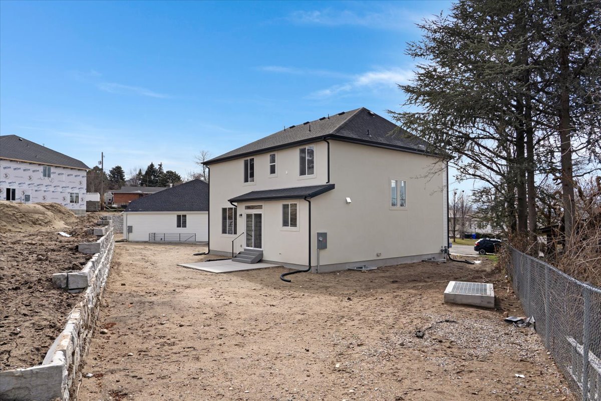 New construction residence featuring a light-colored stucco exterior, a dark shingle roof, and a rear concrete patio