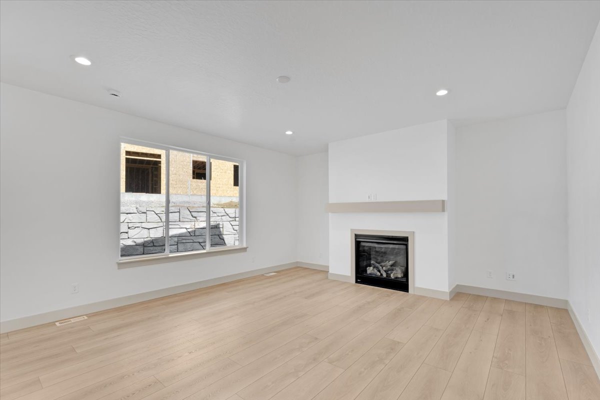 Spacious room featuring light wood-finish flooring, recessed lighting, and a modern fireplace with a light-toned mantel