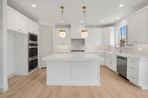 Kitchen featuring a center island, pendant lighting, white cabinets, light wood-type flooring, and stainless steel appliances
