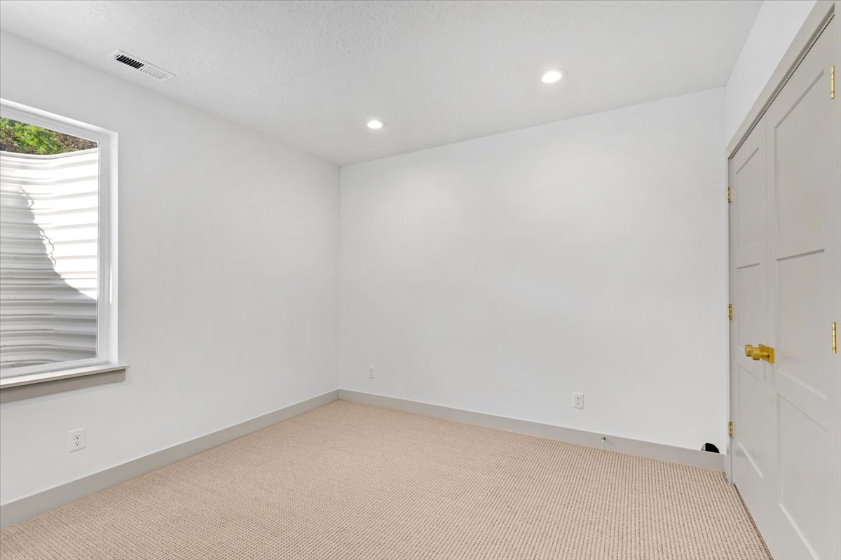 Bright interior space featuring a window with a window well, recessed lighting, neutral carpet flooring, and a two-panel door with gold-toned hardware
