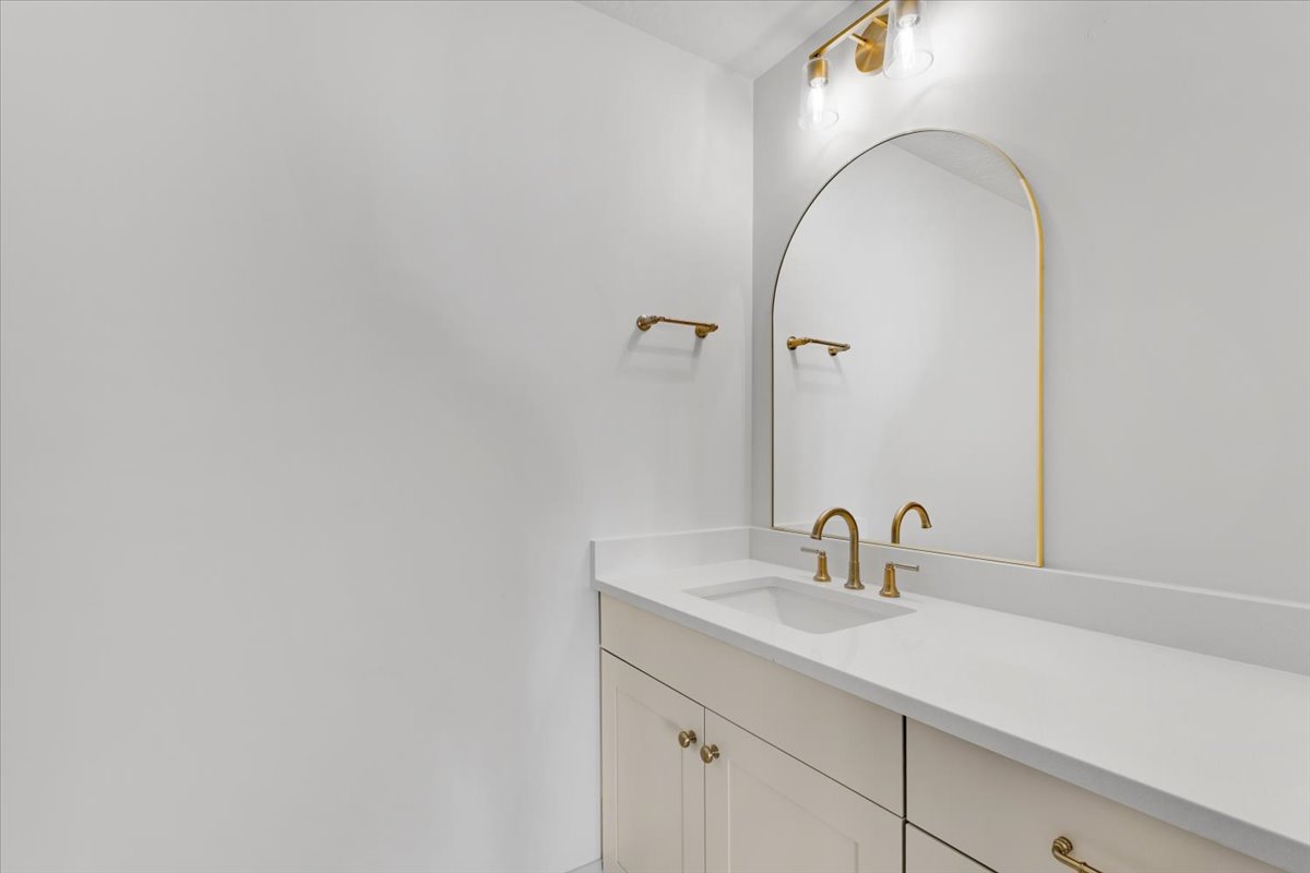 Bathroom vanity featuring a light-toned countertop, undermount sink, and brass-finish faucet