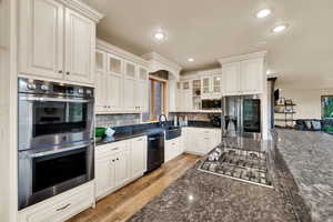 Kitchen featuring appliances with stainless steel finishes, glass insert cabinets, dark stone countertops, backsplash, and recessed lighting