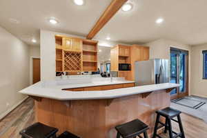 Kitchen with light wood-type flooring, light countertops, a breakfast bar, recessed lighting, and light brown cabinets