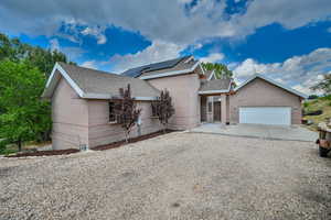 Ranch-style home featuring a shingled roof, brick siding, driveway, roof mounted solar panels, and a garage