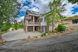 View of front of house featuring a balcony, brick siding, a patio, a shingled roof, and driveway