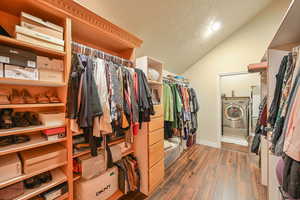 Walk in closet with vaulted ceiling, washer / dryer, and dark wood-type flooring