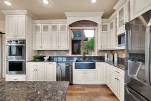 Kitchen featuring appliances with stainless steel finishes, recessed lighting, dark wood-type flooring, dark stone countertops, and glass insert cabinets