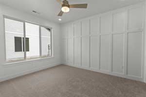 Spare room featuring a decorative wall, carpet floors, and a ceiling fan