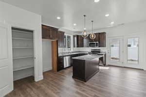 Kitchen with dark brown cabinetry, a center island, decorative light fixtures, stainless steel appliances, and dark wood-style flooring