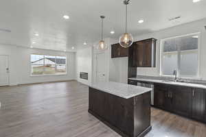 Kitchen featuring dark brown cabinetry, a kitchen island, a large fireplace, light stone counters, and light wood finished floors