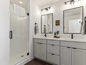 Bathroom with a stall shower, double vanity, and dark wood finished floors