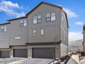 View of snow covered exterior featuring board and batten siding, an attached garage, a mountain view, and driveway