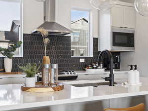Kitchen featuring wall chimney exhaust hood, built in microwave, white cabinets, and light stone counters