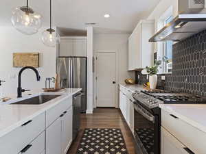 Kitchen with stainless steel appliances, wall chimney range hood, white cabinets, dark wood-style floors, and hanging light fixtures