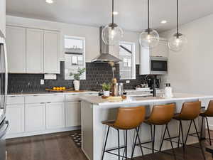 Kitchen featuring a kitchen bar, wall chimney exhaust hood, pendant lighting, and recessed lighting