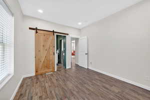 Unfurnished bedroom featuring wood finished floors, a barn door, and recessed lighting