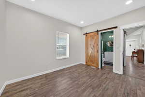 Unfurnished bedroom featuring dark wood-style flooring, a barn door, recessed lighting, and ensuite bathroom