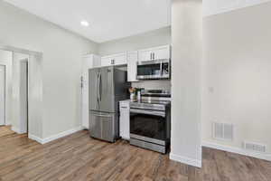Kitchen with appliances with stainless steel finishes, white cabinets, light countertops, and light wood-type flooring