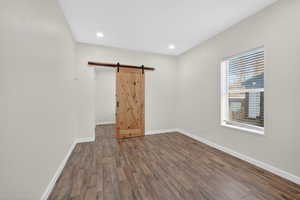 Unfurnished bedroom featuring a barn door, dark wood finished floors, and recessed lighting