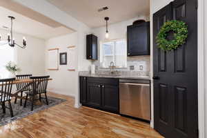 Kitchen featuring light stone counters, dark cabinetry, decorative light fixtures, and stainless steel dishwasher
