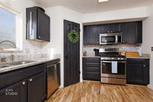 Kitchen with appliances with stainless steel finishes, light stone countertops, backsplash, and light wood-type flooring