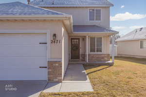 Doorway to property featuring covered porch, a lawn, a garage, stucco siding, and brick siding