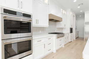 Kitchen with built in appliances, white cabinetry, glass insert cabinets, light wood finished floors, and recessed lighting