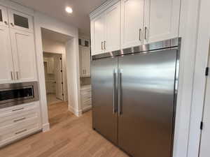 Kitchen with built in appliances, white cabinetry, glass insert cabinets, and recessed lighting