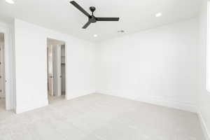 Unfurnished bedroom featuring recessed lighting, a walk in closet, a decorative wall, light carpet, and ceiling fan