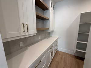 Bar area featuring open shelves, white cabinets, light wood-style flooring, and glass insert cabinets