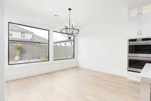 Unfurnished dining area featuring suspended lighting, light wood-type flooring, and wooden walls
