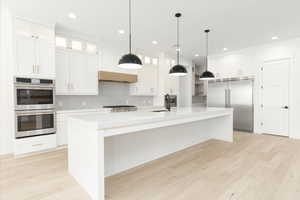 Kitchen with light wood-type flooring, white cabinets, stainless steel appliances, a large island, and pendant lighting