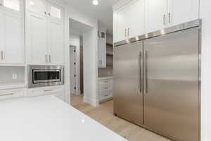 Kitchen with built in appliances, white cabinets, glass fronted cabinets, light wood finished floors, and recessed lighting