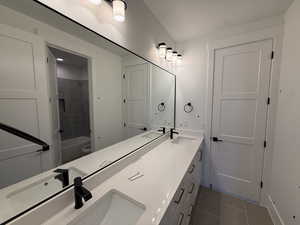 Full bathroom with double vanity, tub / shower combination, and dark tile patterned flooring