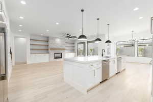 Kitchen with open floor plan, a stone fireplace, a chandelier, white cabinets, and an island with sink
