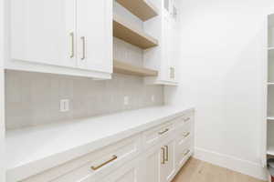 Kitchen featuring open shelves, white cabinetry, light wood-style flooring, backsplash, and glass fronted cabinets