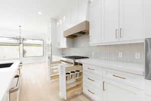 Kitchen with white cabinetry, light stone counters, light wood finished floors, glass fronted cabinets, and backsplash