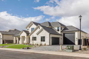 View of front facade with board and batten siding, a garage, driveway, and stone siding