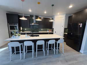 Kitchen featuring a kitchen breakfast bar, modern cabinets, black appliances, wall chimney exhaust hood, and pendant lighting