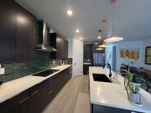 Kitchen with modern cabinets, hanging light fixtures, dark cabinets, a textured ceiling, and wall chimney exhaust hood