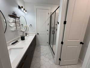 Full bath featuring double vanity, light tile patterned flooring, and a stall shower