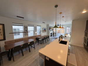 Kitchen featuring hanging light fixtures, a kitchen island with sink, a textured ceiling, a glass covered fireplace, and open floor plan