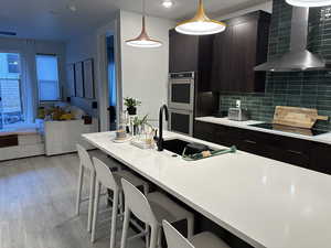 Kitchen with modern cabinets, wall chimney range hood, a kitchen bar, and light wood-type flooring