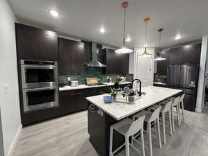 Kitchen featuring appliances with stainless steel finishes, a kitchen bar, modern cabinets, a kitchen island with sink, and hanging light fixtures