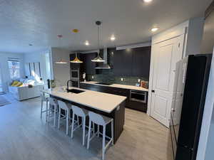 Kitchen with a textured ceiling, a breakfast bar, hanging light fixtures, black appliances, and a center island with sink