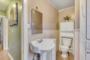 Bathroom featuring a wainscoted wall, crown molding, and light tile patterned floors