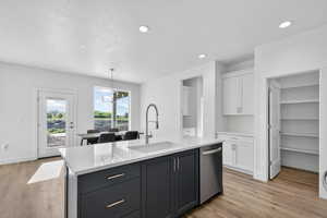Kitchen featuring two tone color scheme, light wood finished floors, an island with sink, light stone counters, and stainless steel dishwasher